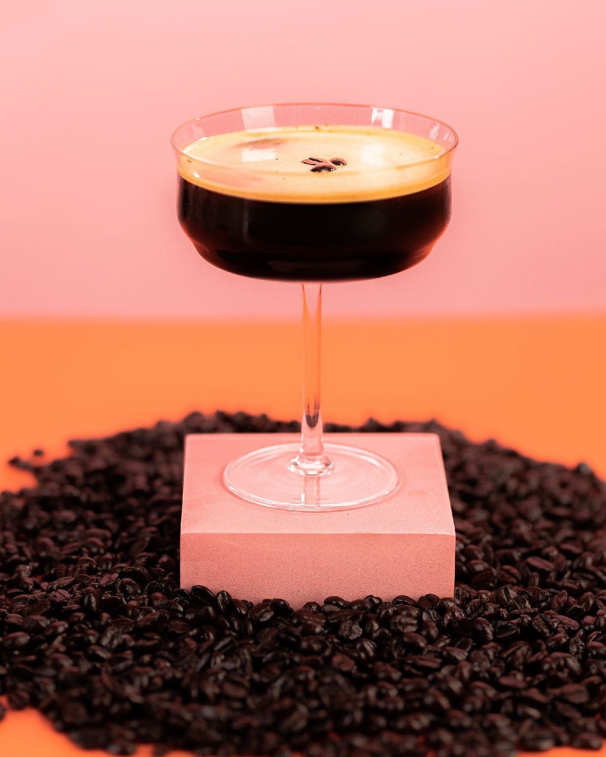THC espresso martini in a coupe glass with a crema top and espresso beans, standing on a bed of coffee beans against a pink backdrop