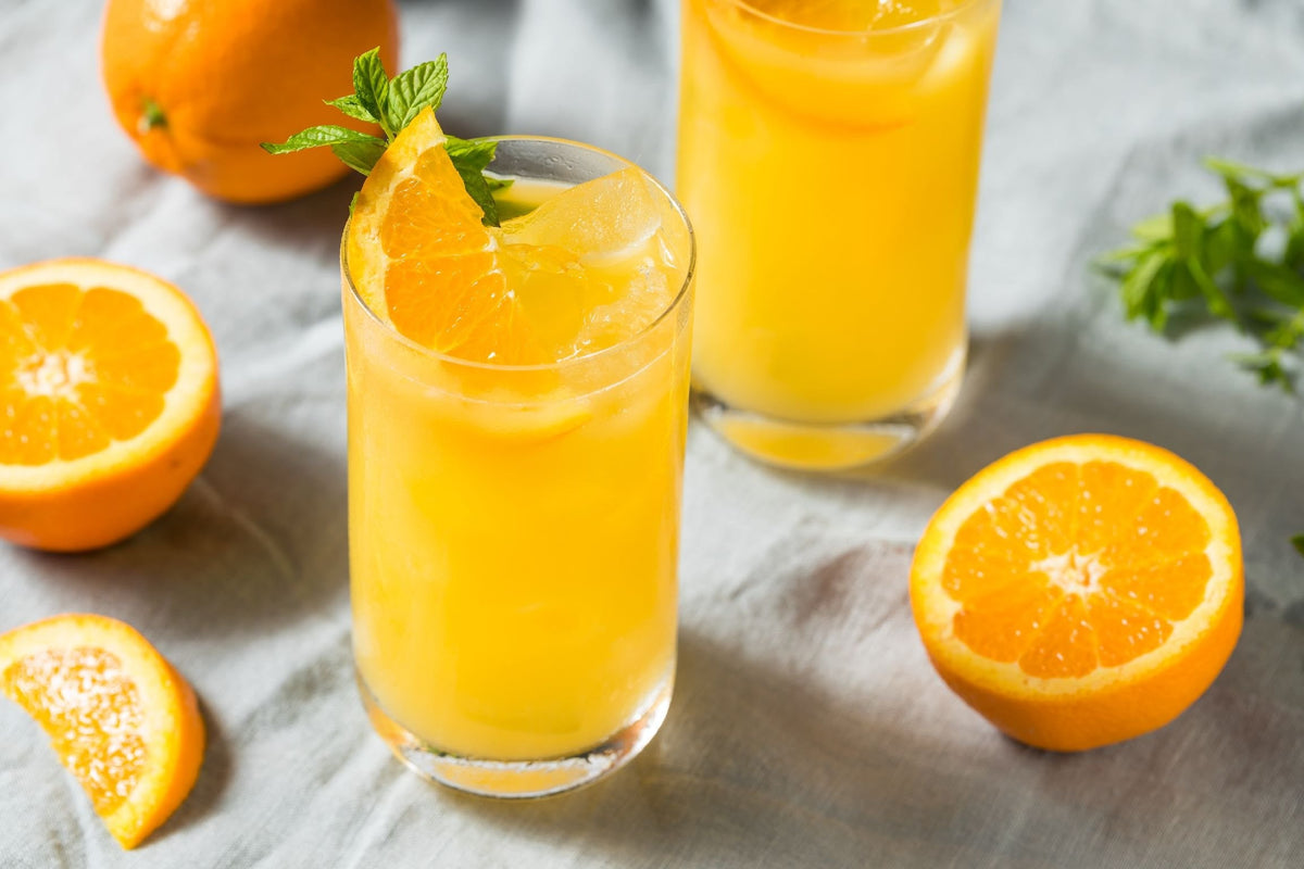 Flora Screwdriver THC cocktail in two glasses of fresh orange juice over ice, garnished with mint and orange slices