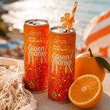 Two cans of Green Monke Skinny Amalfi Spritz THC & THCV cocktails are displayed on a beach table with oranges, a net, and a striped umbrella in the background.